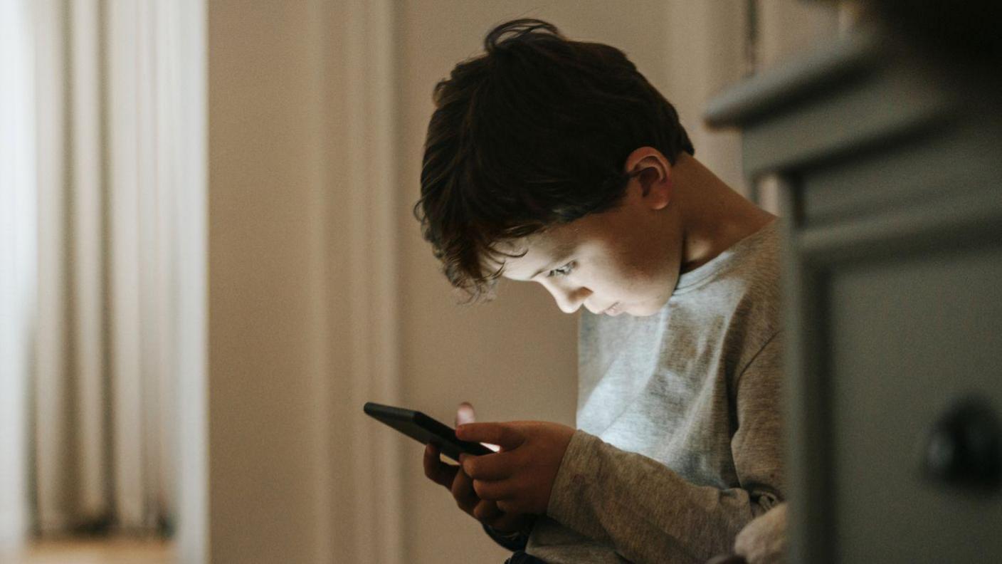 A young boy stares down at a smartphone.