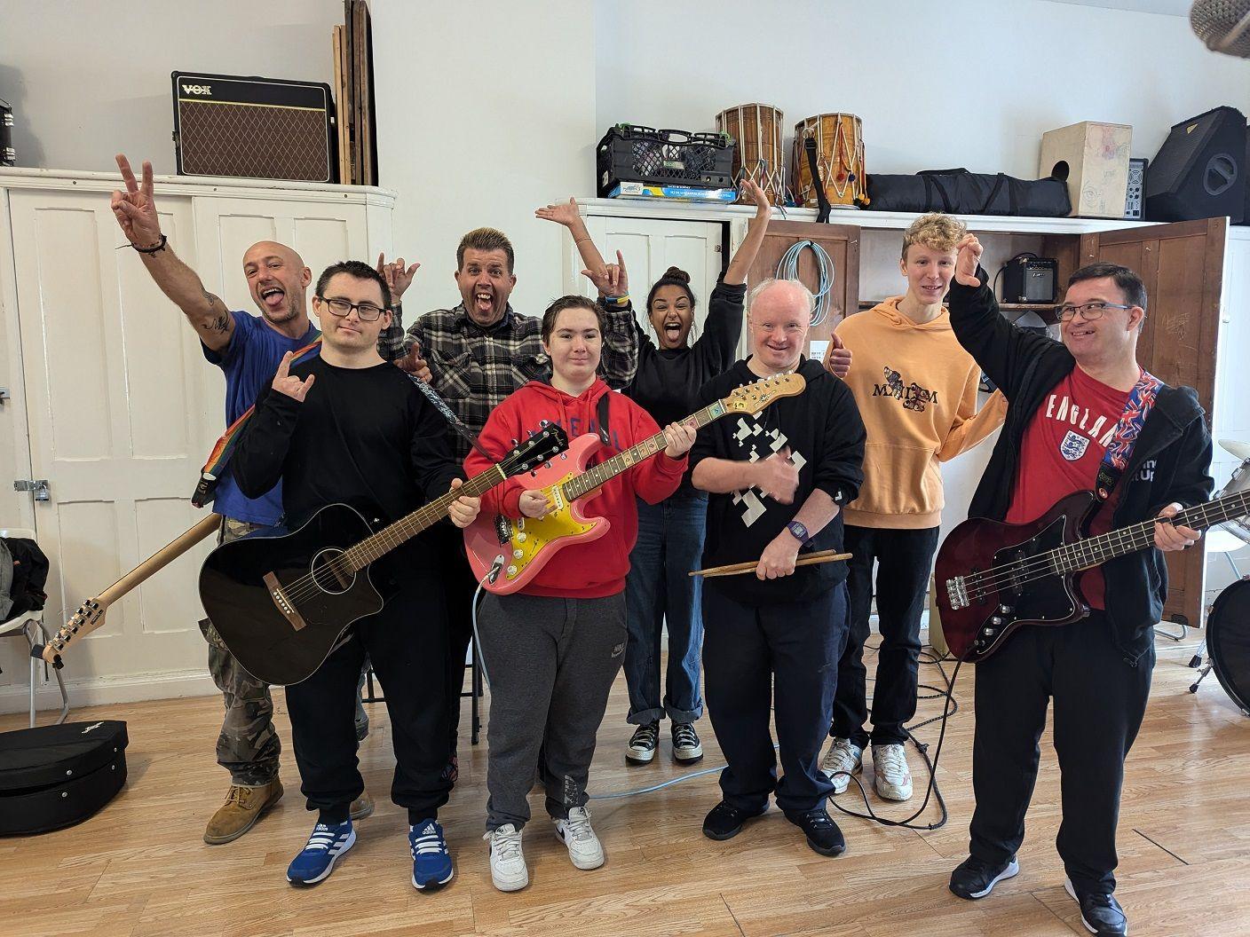 A group of musicians inside a room, some holding guitars and others waving their hands and doing High fives