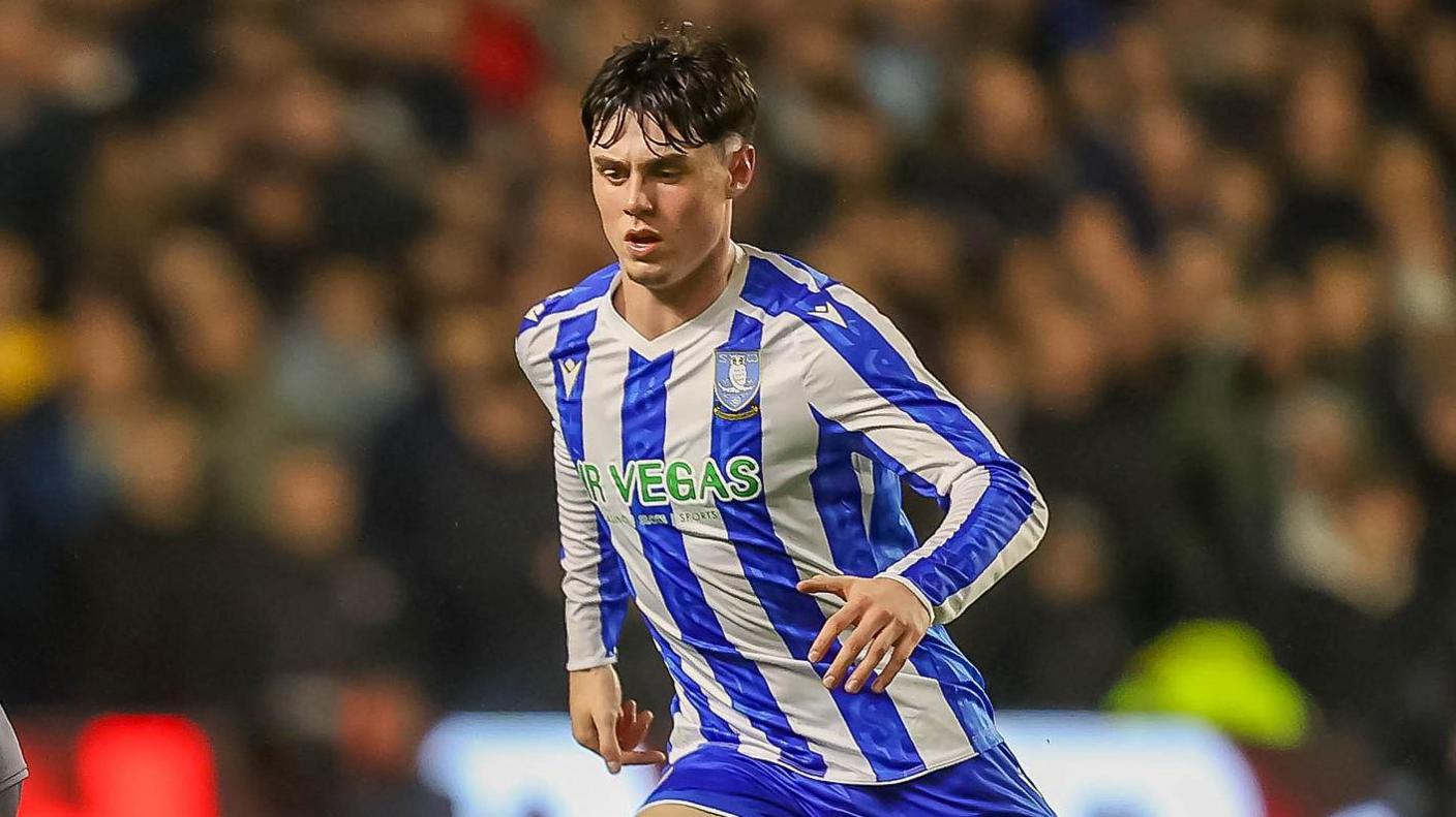 George Brown has a determined look on his face with his brow furrowed with his gaze towards the floor. He is running. He wears a blue and white vertically striped Sheffield Wednesday shirt.