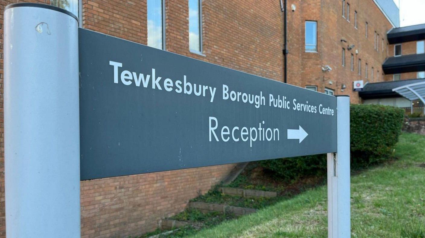 A picture of a grey sign outside the Tewkesbury Borough Council building wall reading 'Tewkesbury Borough Public Services Centre Reception'