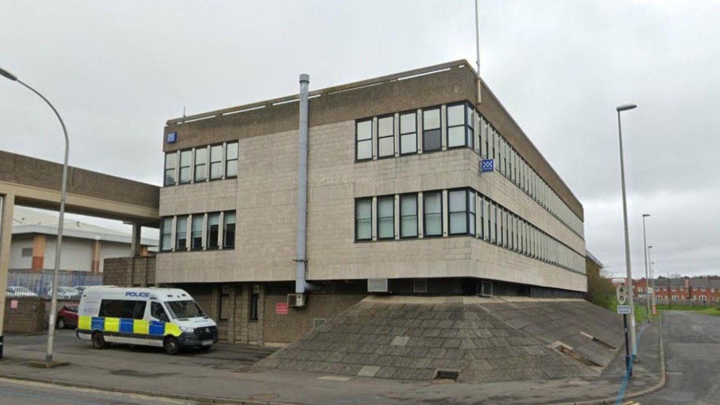 Washington Police Station. It is a light grey three-storey building. A police van is parked outside. 