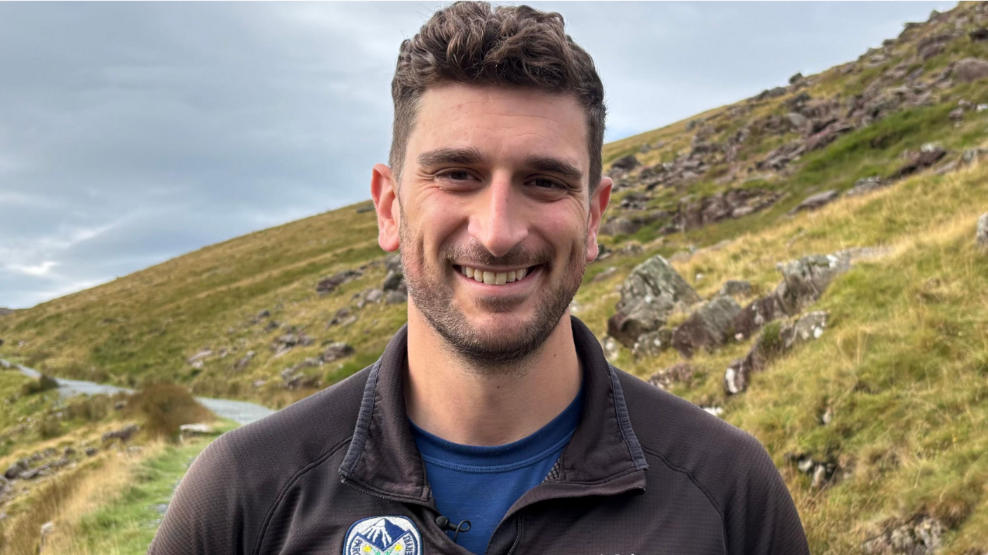 Alun Jones, warden ardal gyda Pharc Cenedlaethol Eryri yn sefyll ar lethrau'r Wyddfa