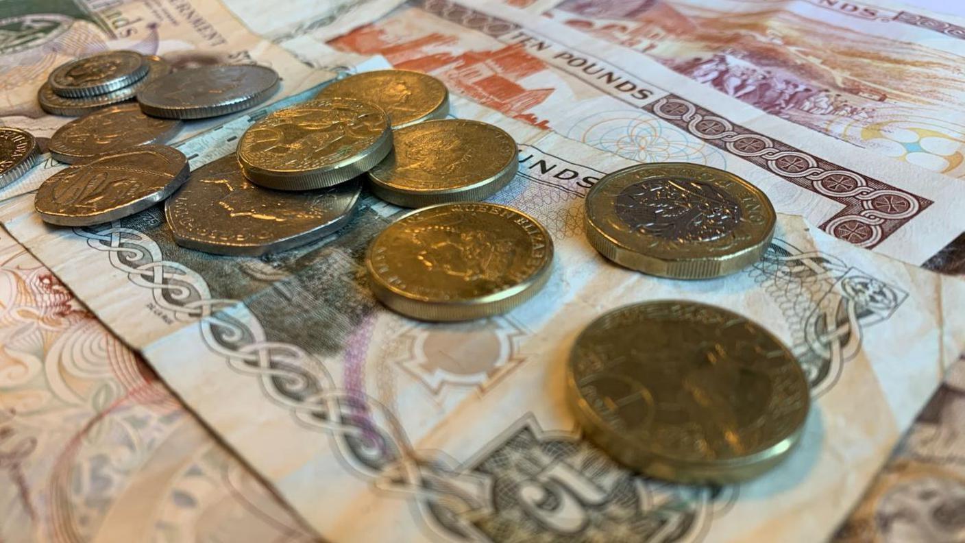 Loose change laid on top of a number of Manx £5 and £10 notes that have been spread out.