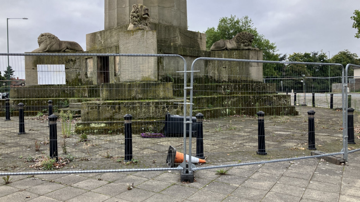 Metal barriers surround the base of the stone statue and column.