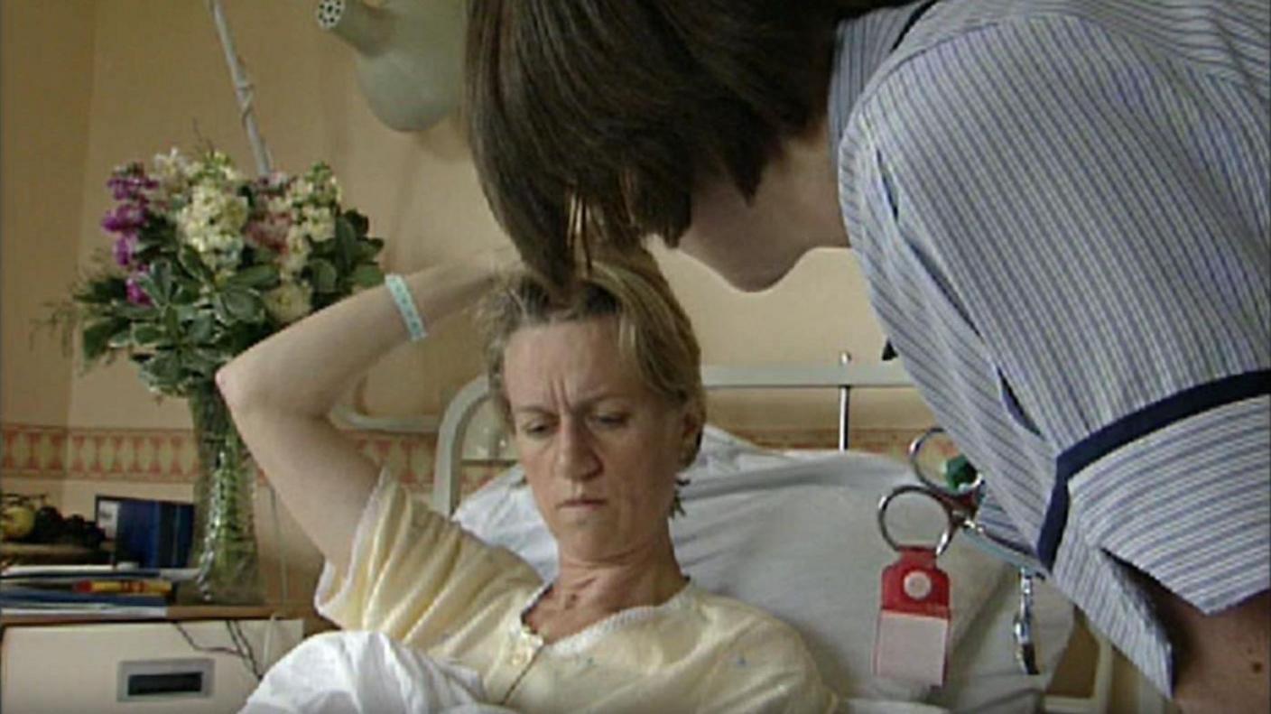 Sally Taylor in hospital in 1999. She is in a hospital bed being tended to by a nurse.