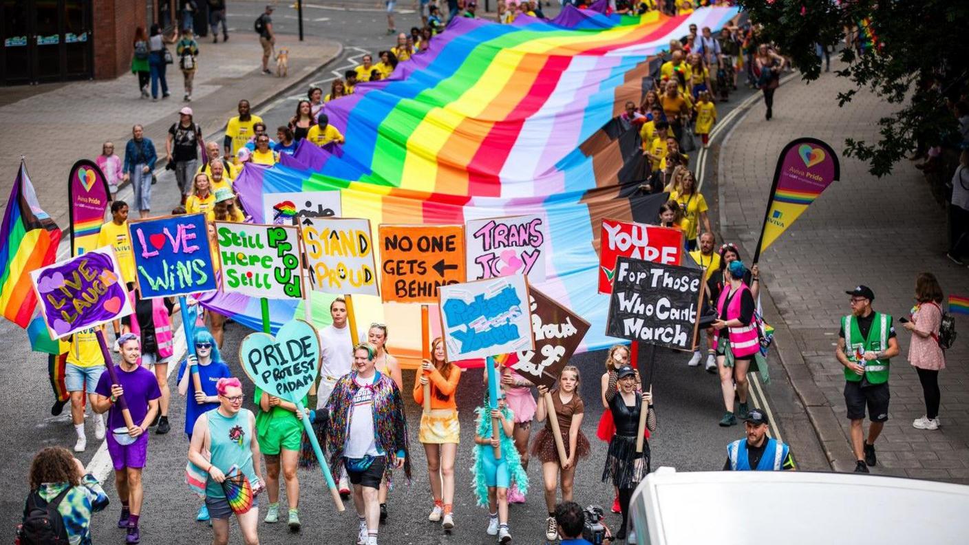 A group of people carrying a large pride flag through the streets 