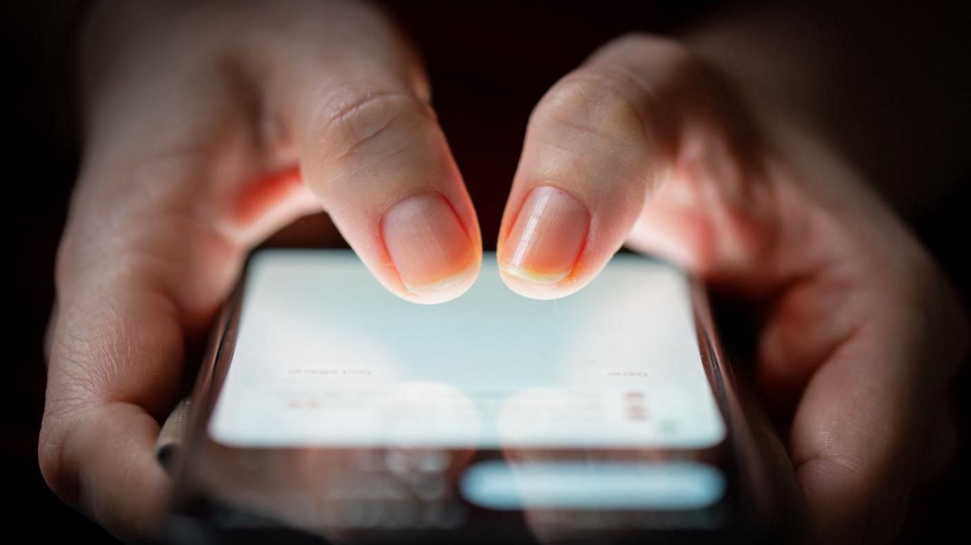 A close up of hands holding a mobile phone. The screen is on. 