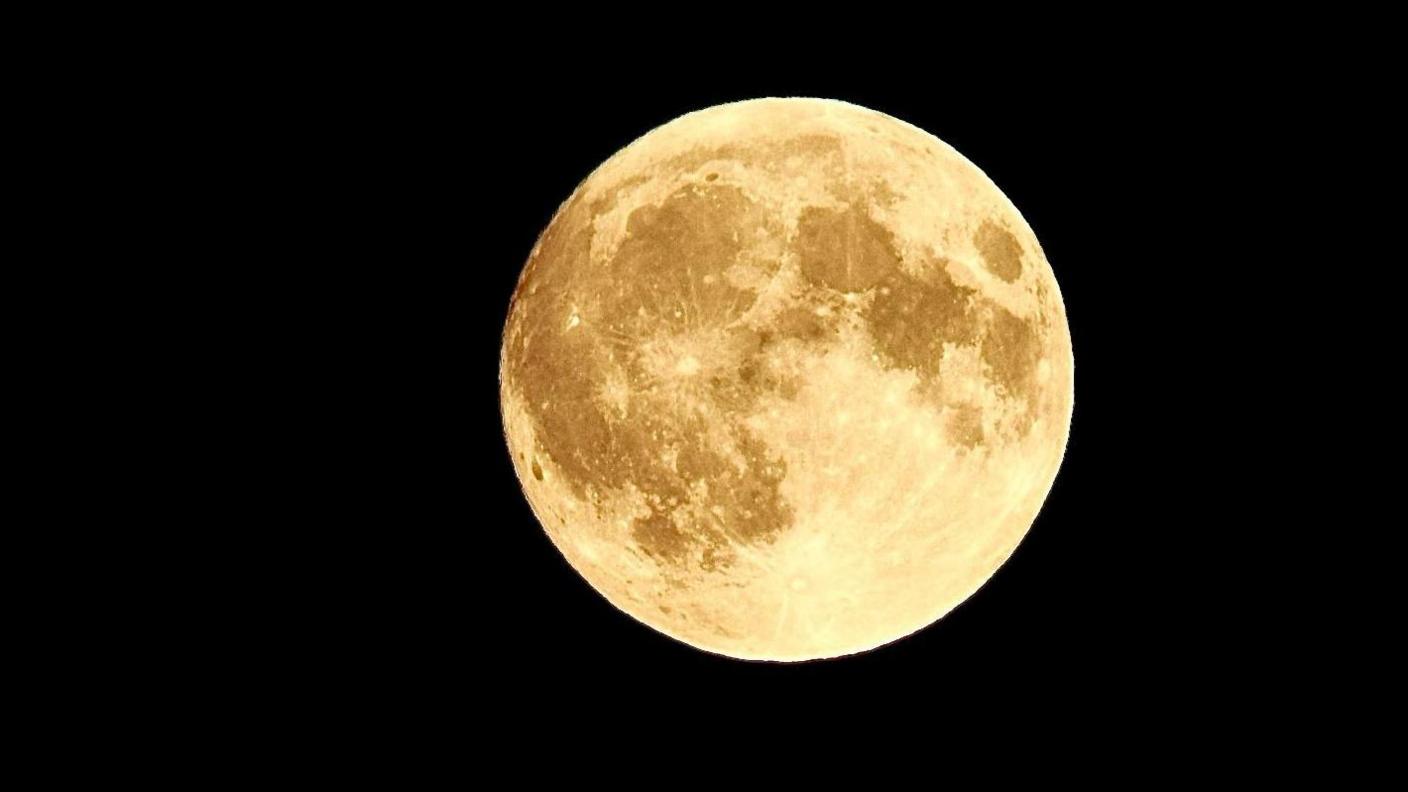 An orange moon hanging over the sky in Telford, Shropshire. It is against a black background. 