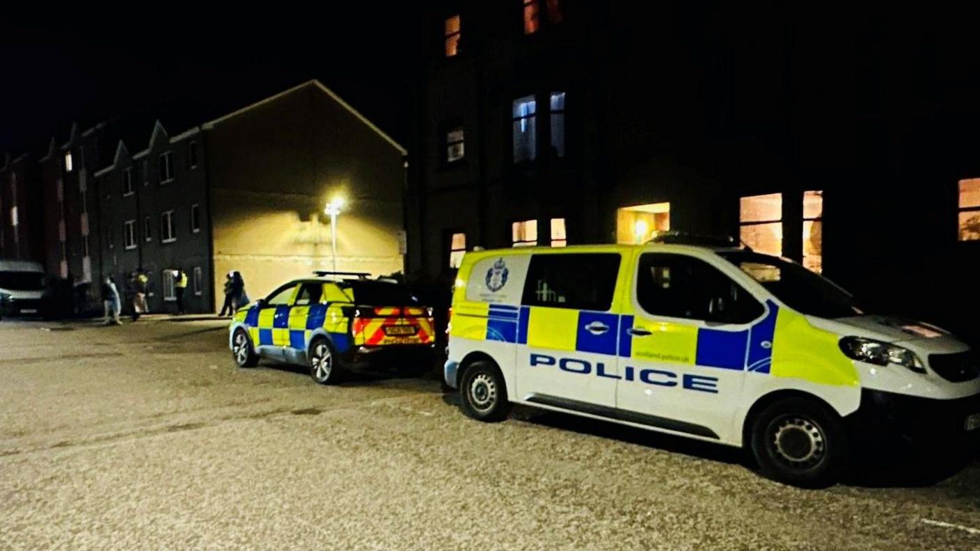 Police vehicles outside Farmer's Hall in Aberdeen, in the dark.
