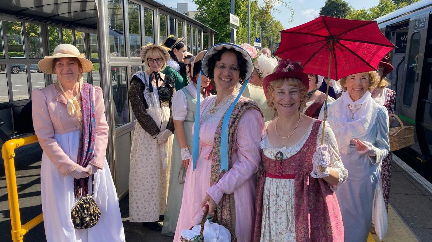 A group of ladies in Regency fancy dress stand on a train platform as they visit the Jane Austen Festival in Bath