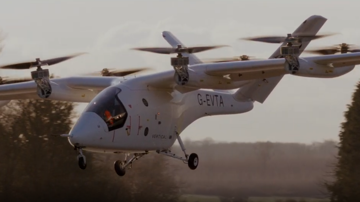 A small white aircraft, which looks like a cross between a helicopter and a small airplane. It has small helicopter-like propellers along its wing span. 