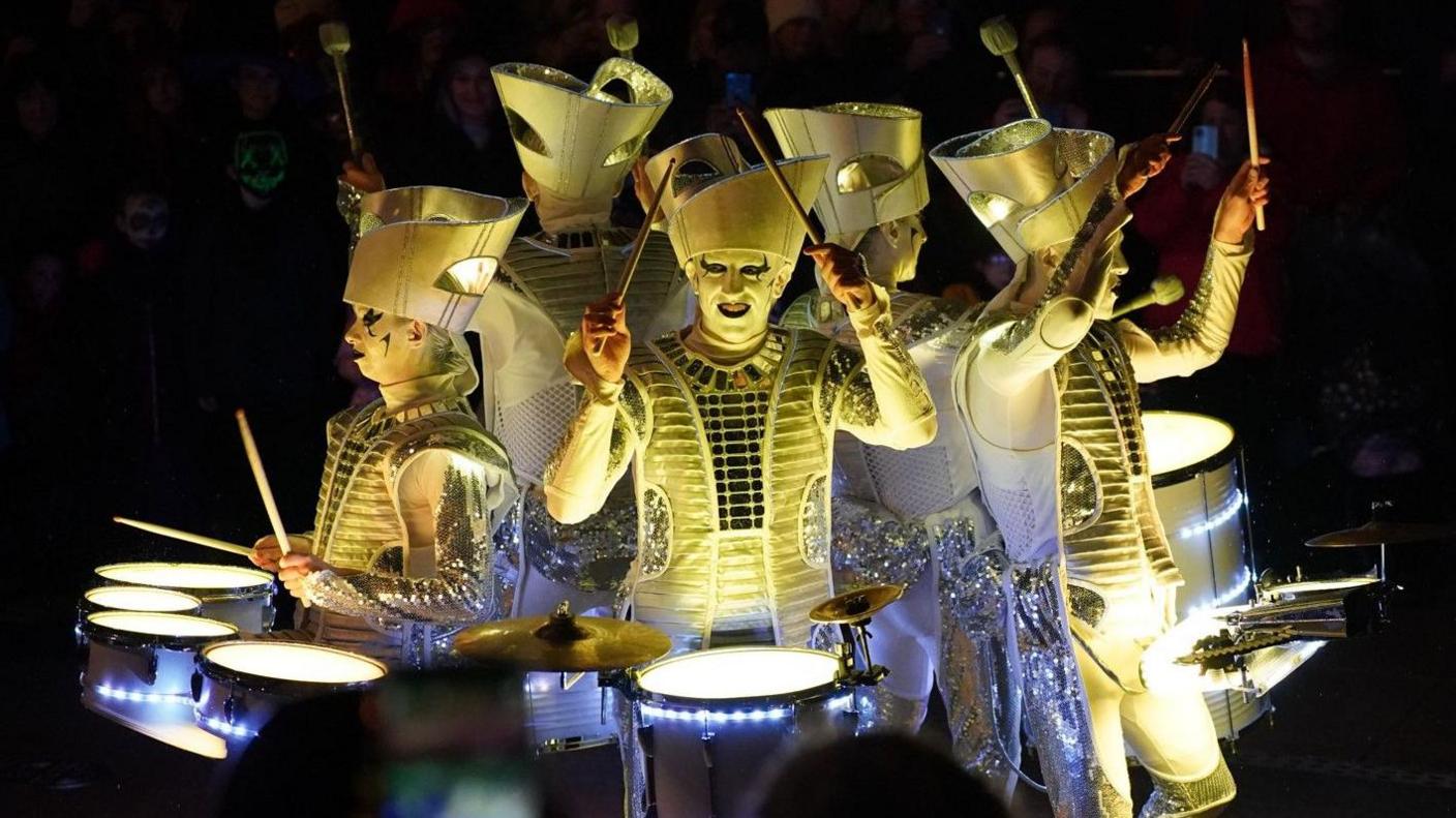 Five performers, dressed in elaborate white costumes, pictured playing drums during the Derry Halloween parade in Londonderry in 2022