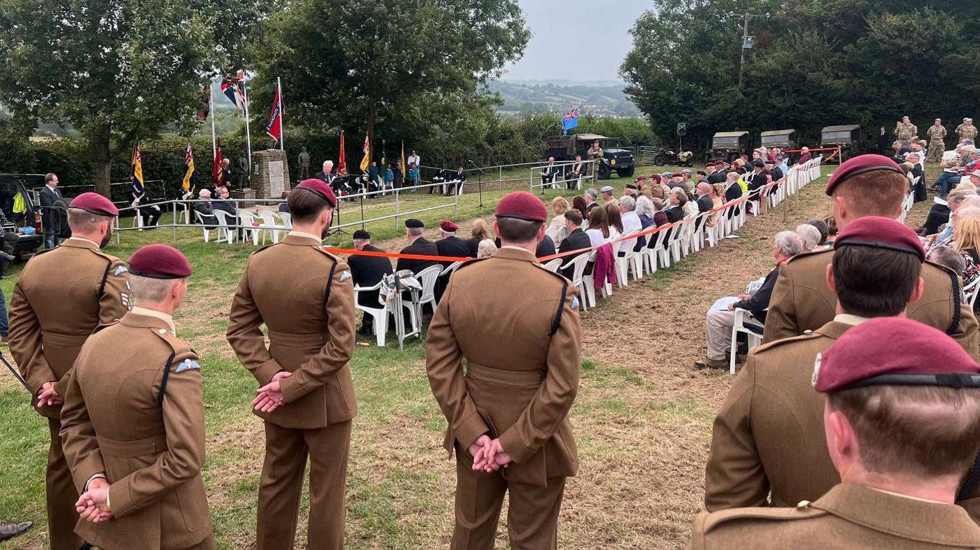 A group of men in military uniforms with red berets watch over a large crowd gathered for a memorial event in Farrington Gurney near Bristol