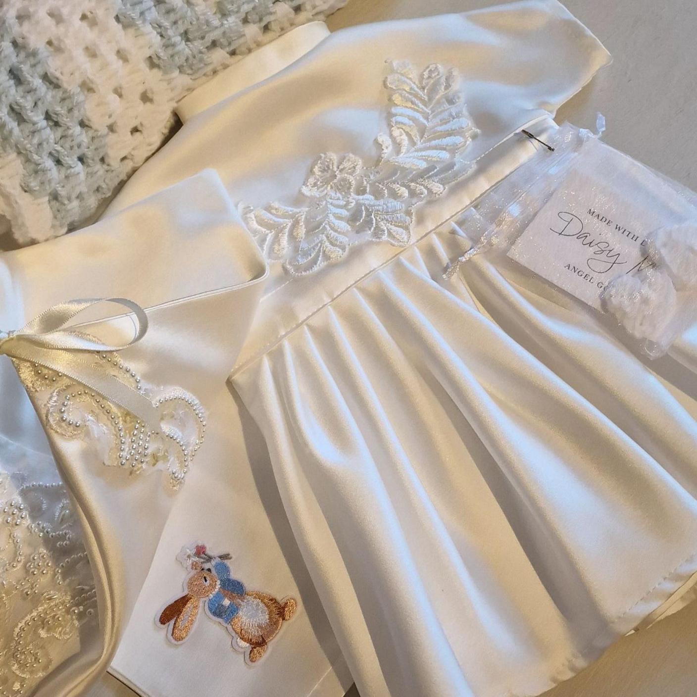 A little white gown with a pattern on the front along with a picture of Peter Rabbit and a nametag that says Daisy.