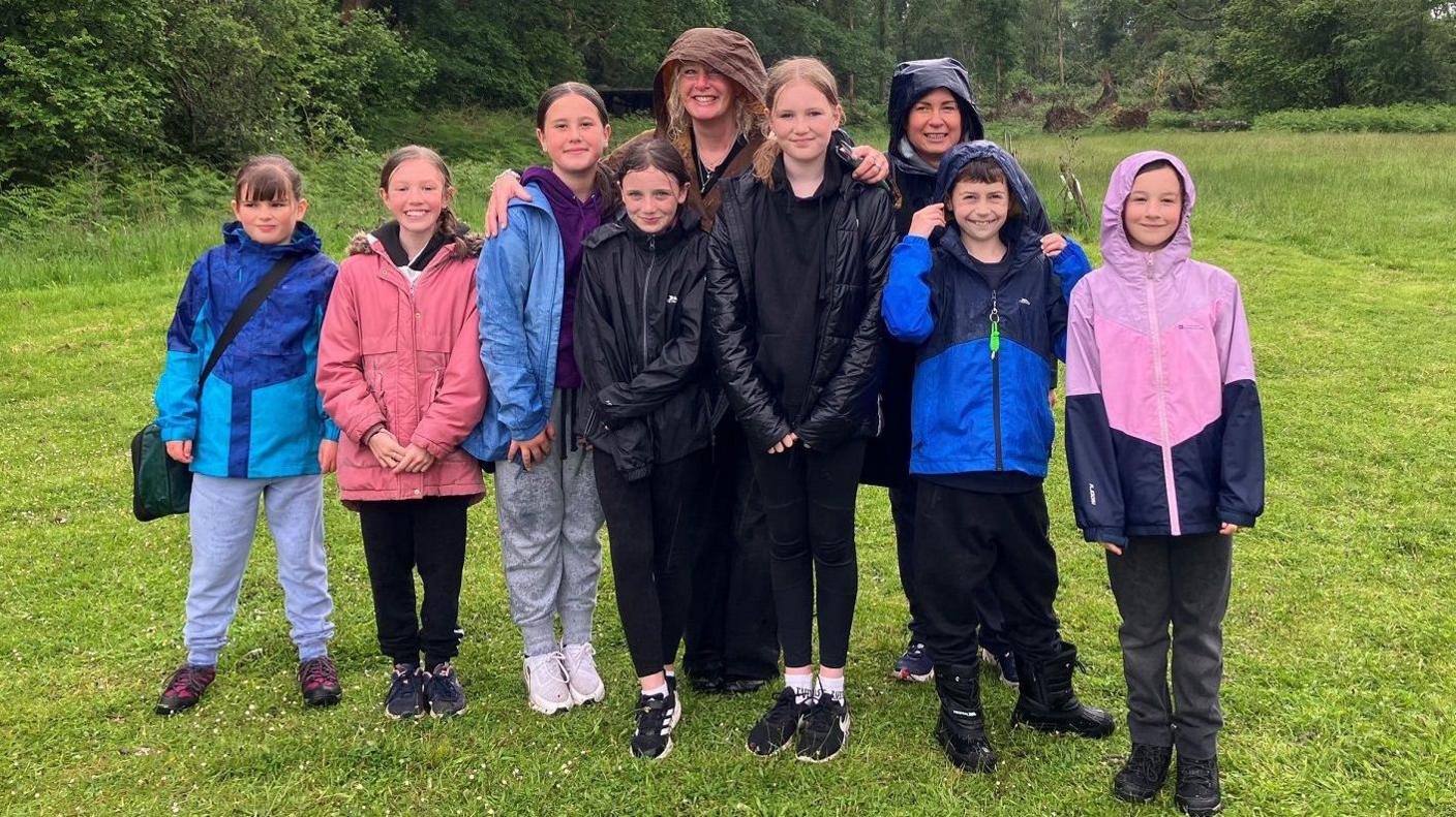 Group of seven children with two adults stood in rainy field smiling