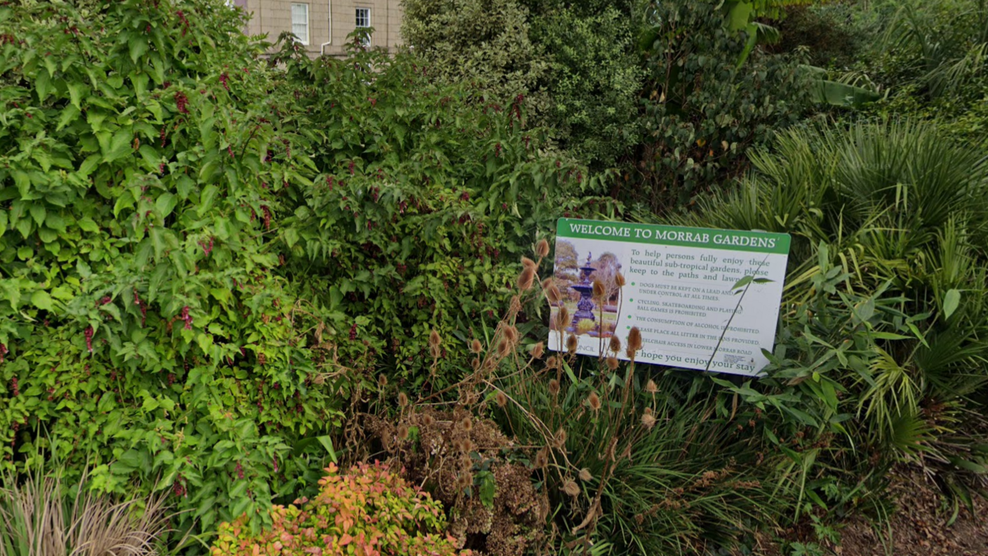 A sign reading 'Welcome to Morrab Gardens' resting in a bed of tropical shrubs.