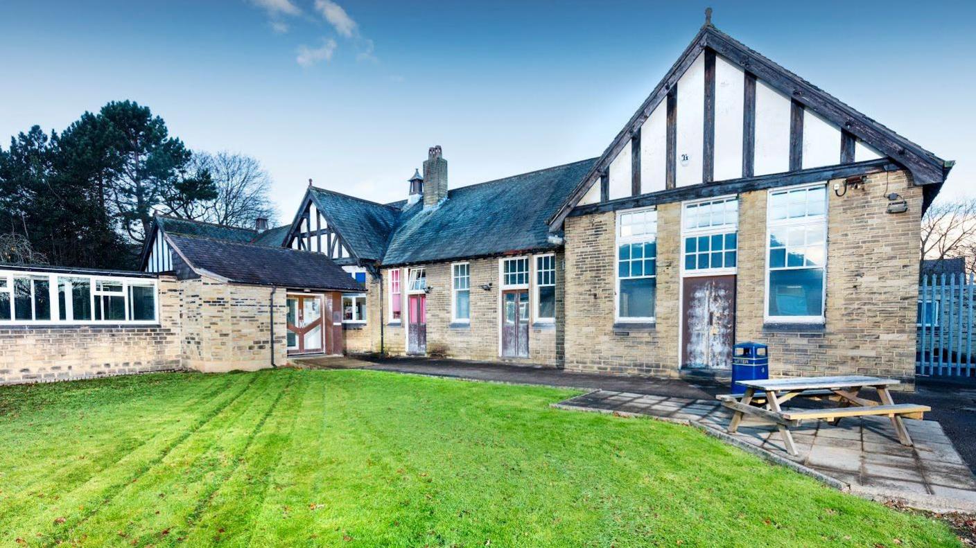 A single-storey hospital building with wooden timbers on the front, and a tidy mown lawn in the foreground.