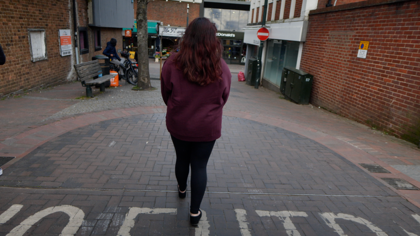 Jane walking down the street in the middle of the day with her back facing the camera