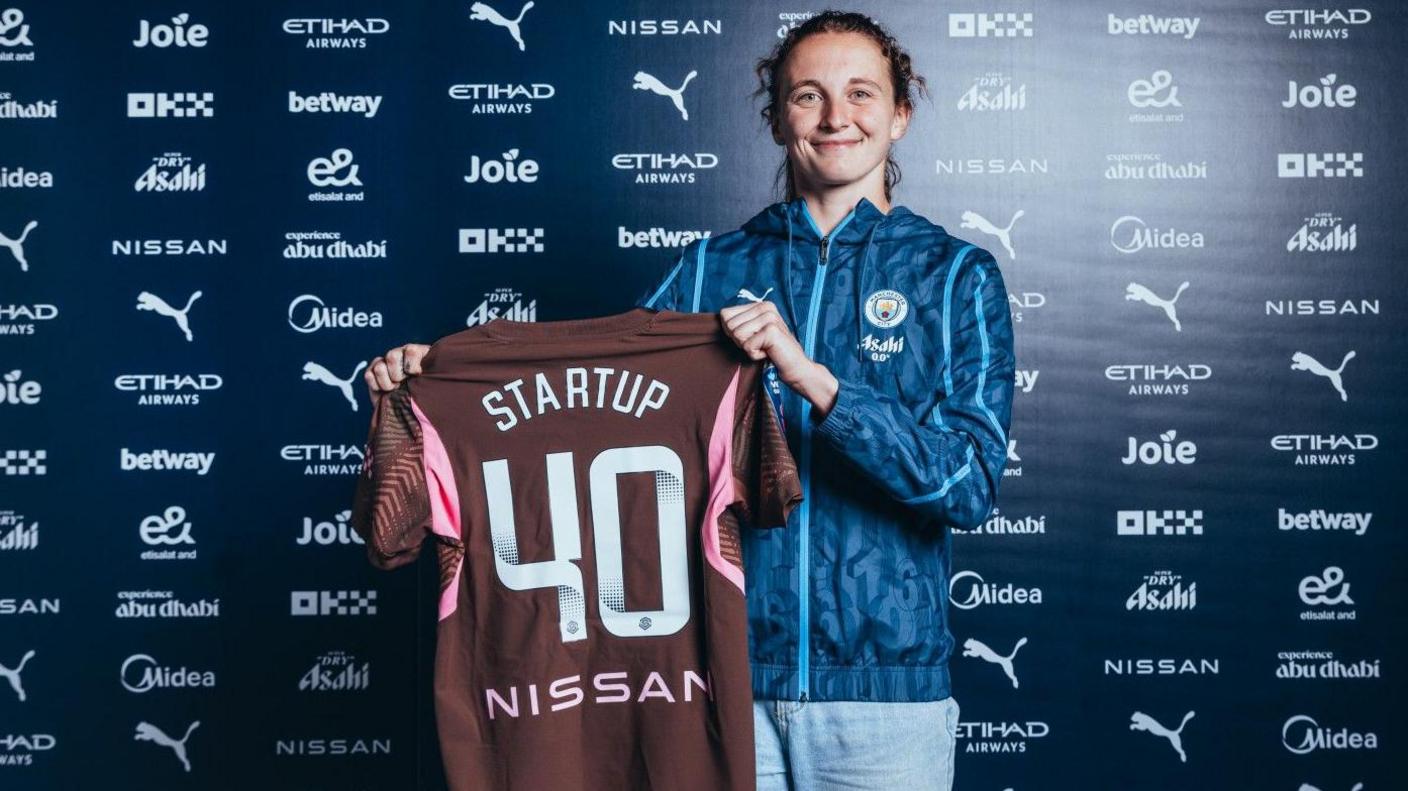 Katie Startup holds up a Manchester City shirt 