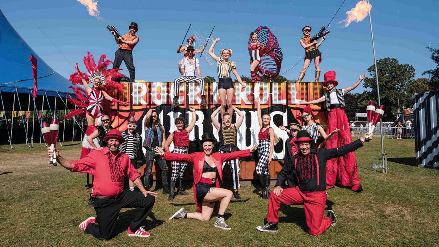 Acrobats standing in front of and on a large sign that reads "Rock N Roll Circus"