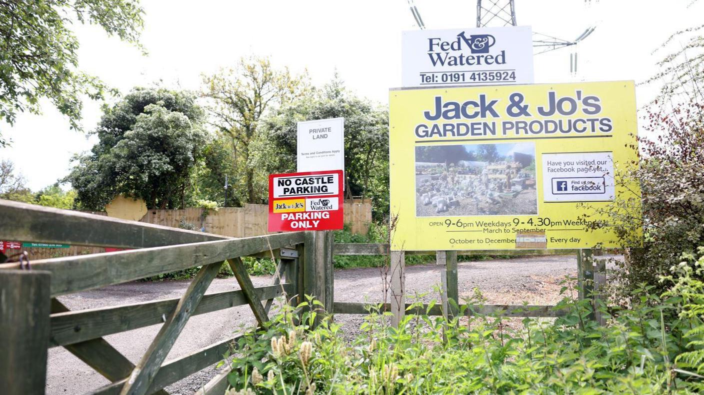 A sign for Fed & Watered cafe. It stands above another sign for Jack & Jo's Garden products. The site's gravel car park is located behind a wodden fence behind the signs.