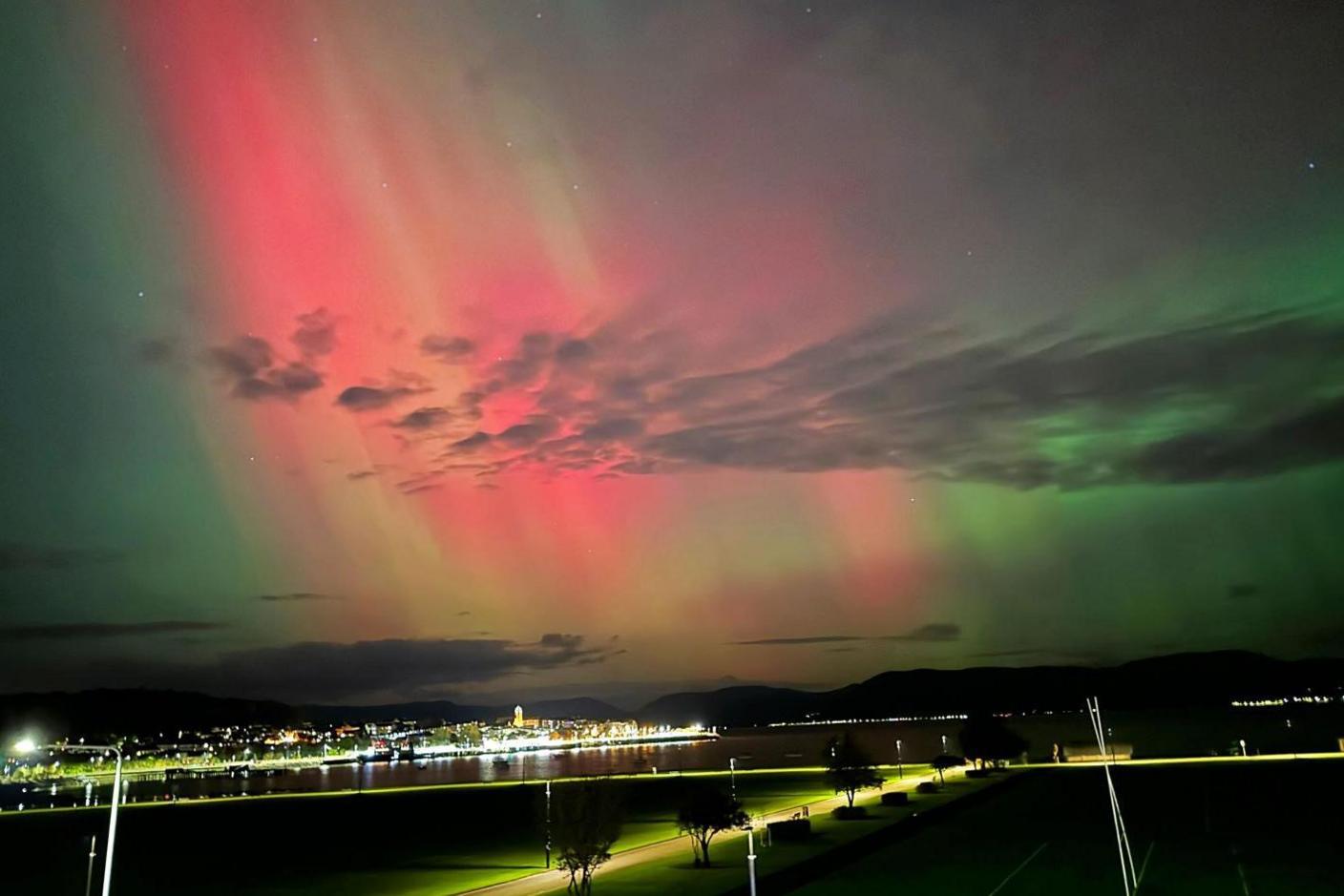 The aurora appears as a curtain of light in pinks and greens behind cloud and above street lights.