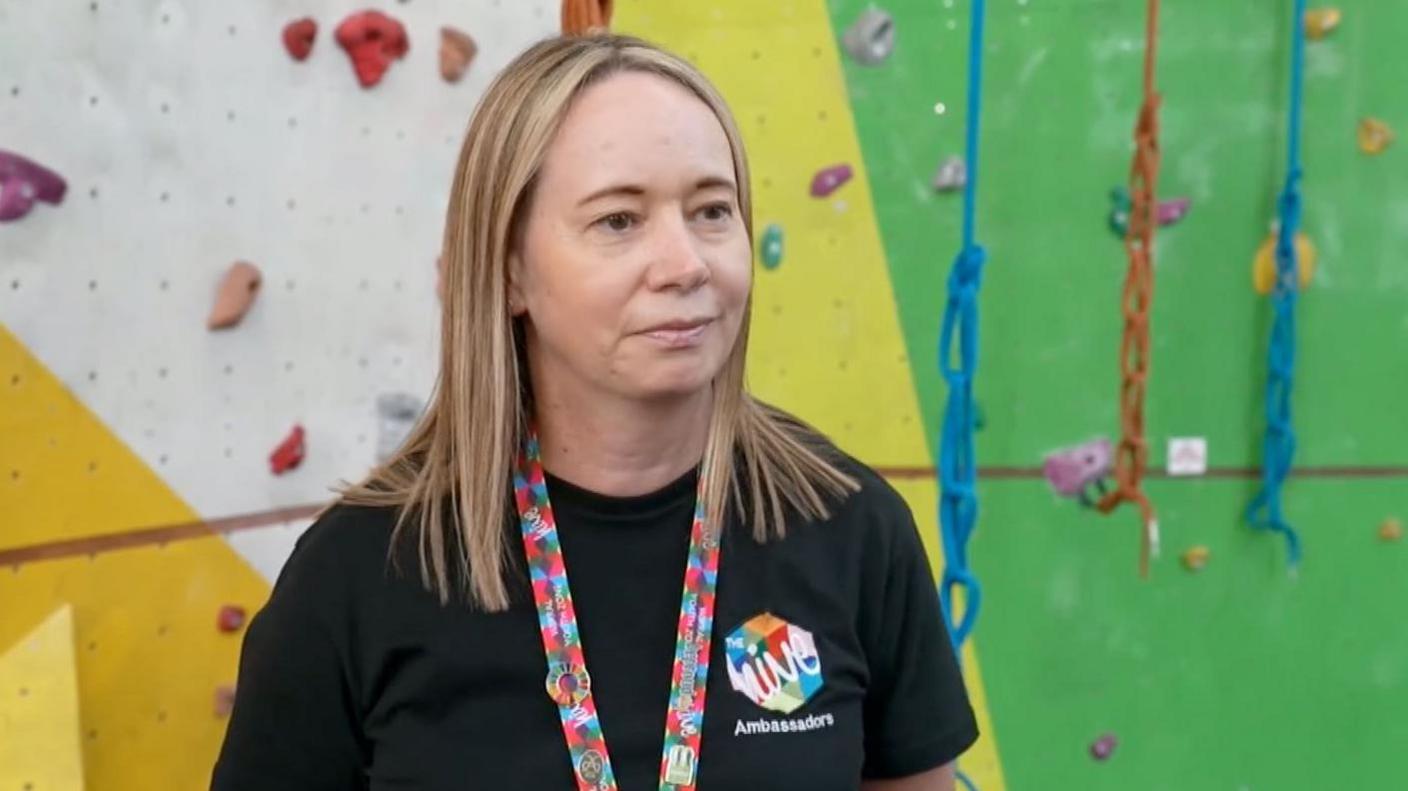 Bex Pollard has long highlighted blonde hair. She is wearing a Hive-branded black t-shirt and a multi-coloured lanyard around her neck.