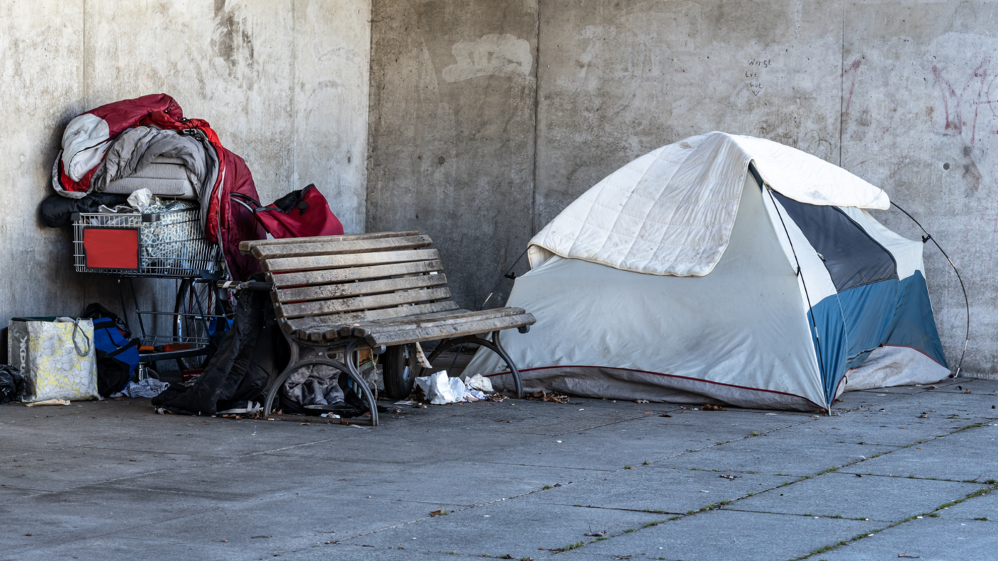 A tent and a shopping trolley loaded with possessions beside a park bench.