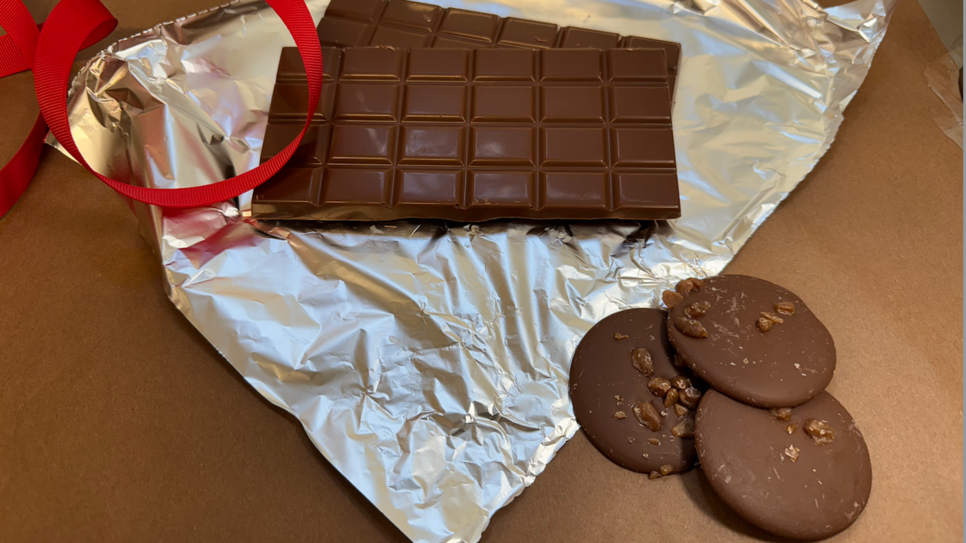 Two chocolate bars on foil and some giant chocolate buttons with them red ribbon nearby