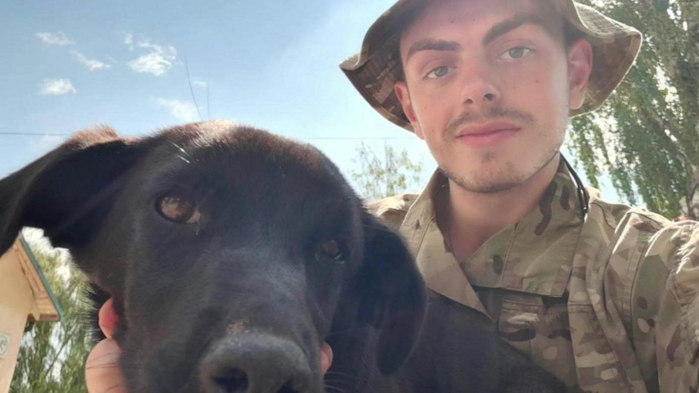 Mr Tindal-Draper wearing camouflage clothing while holding a black dog 