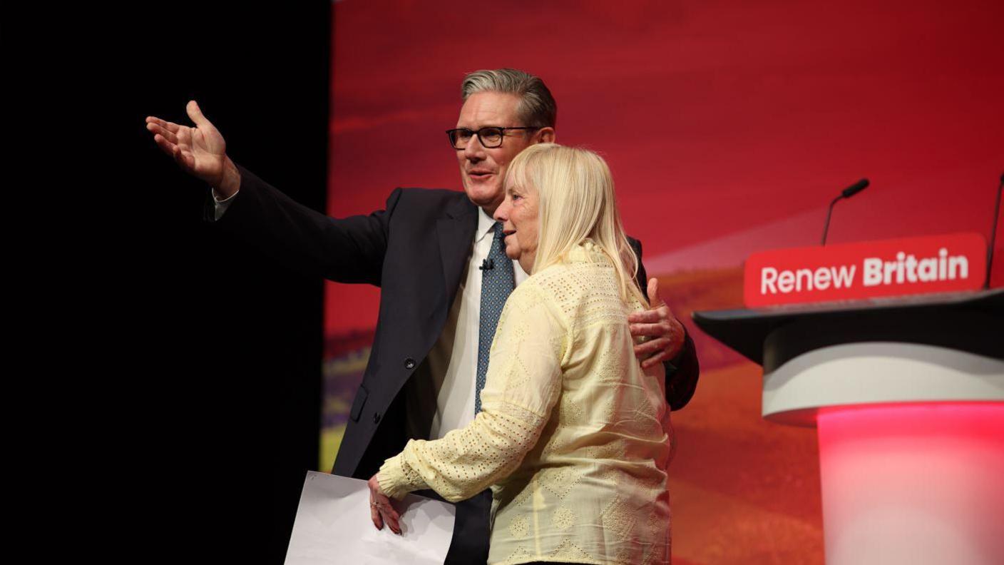 Sir Keir Starmer stands on a stage at the Labour party conference with his arm around Margaret Aspinall 