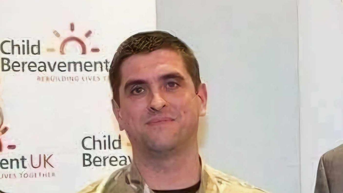 Trevor Bygate in Army uniform stands in front of a poster wall that reads "Child Bereavement UK"