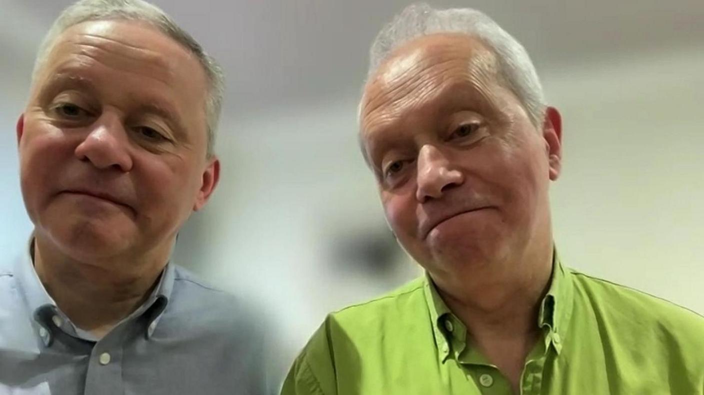 A screenshot of a Zoom interview with Fr Martin O'Hagan and Fr Eugene O'Hagan. Fr Martin is on the left, with short grey hair and wearing a blue, buttoned-up shirt. On the right is Fr Eugene with grey hair, wearing a green, button-up shirt.