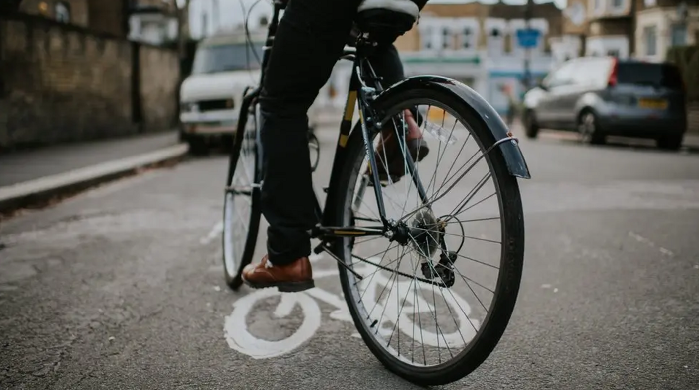 An image of a cyclist on a bike. The image is taken from behind them and only the back of their lower legs straddling the bicycle in the road are visible. 