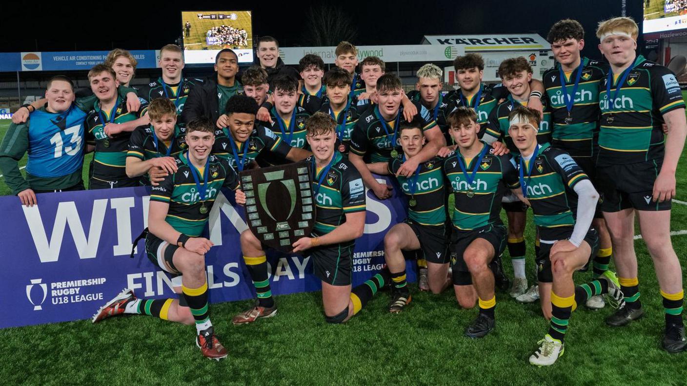 Northampton Saints' Academy team pose with the Academy trophy on the touchline 