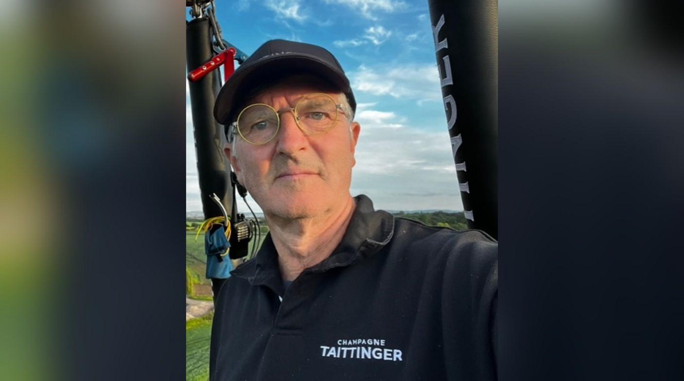 Pete Dalby. He is wearing a black hat and reading glasses. He is pictured in a hot air balloon. He is looking at the camera and squinting in the sun.