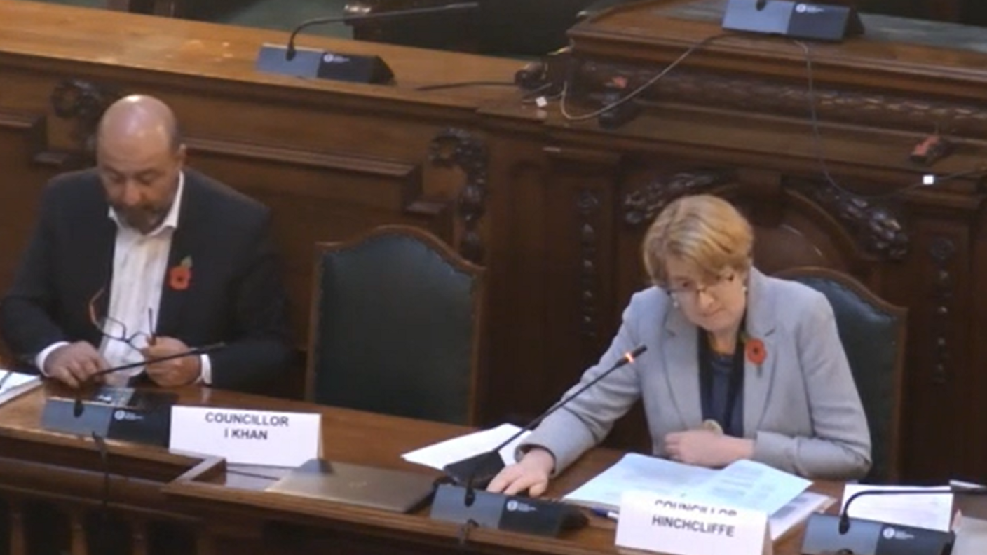 Susan Hinchliffe wears a grey jacket and sits in a large chair in a dark wood panelled room at Bradford Council meeting