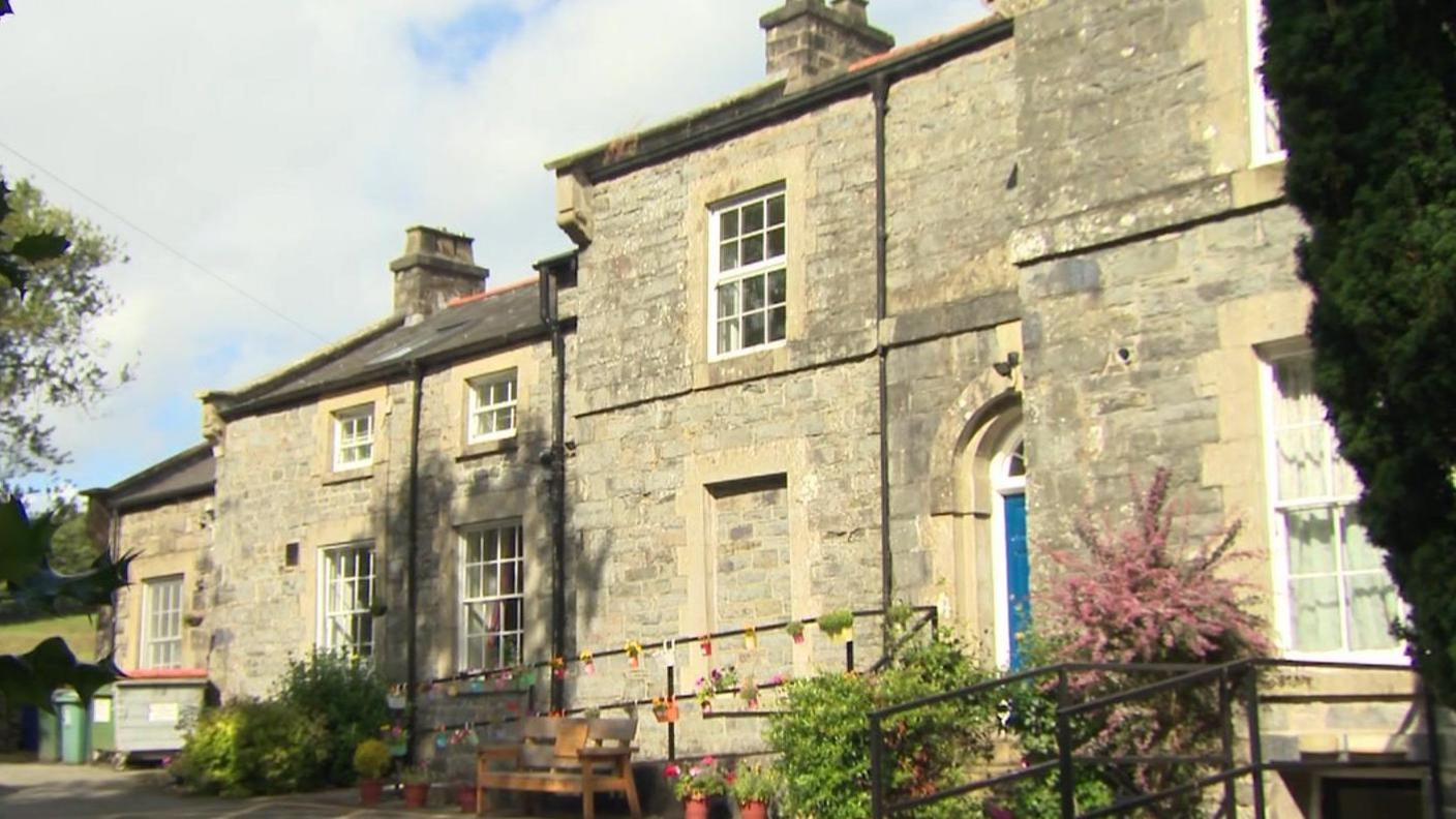 Care home in Pentrefoelas - a large stone building with railings near the front entrance, with trees nearby and a field in the distance 