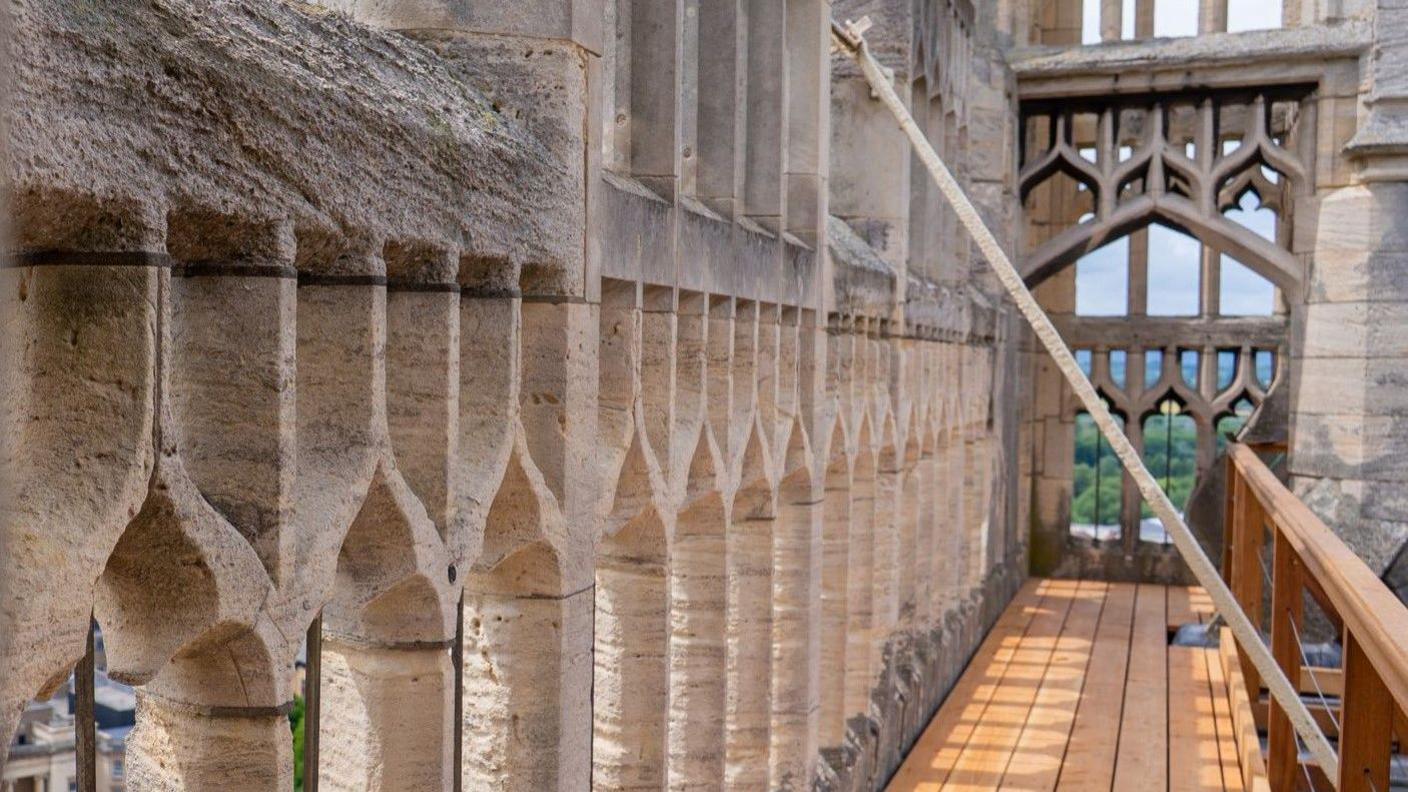 A photo showing a wooden walkway next to the stone wall of a cathedral tower