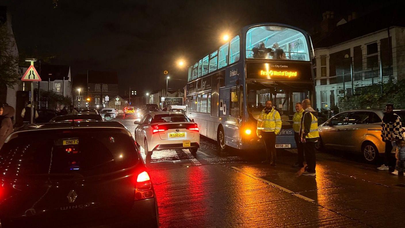 A bus in the street at night with people standing by it