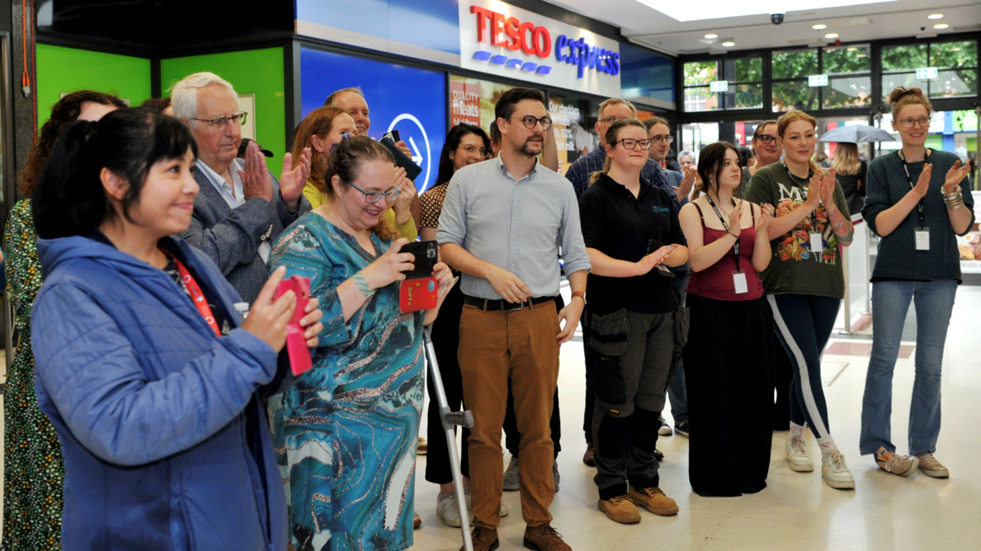 About a dozen people gathered together in a shopping centre, several holding cameras, and all watching the launch of the new hub, which is going on to the right of camera