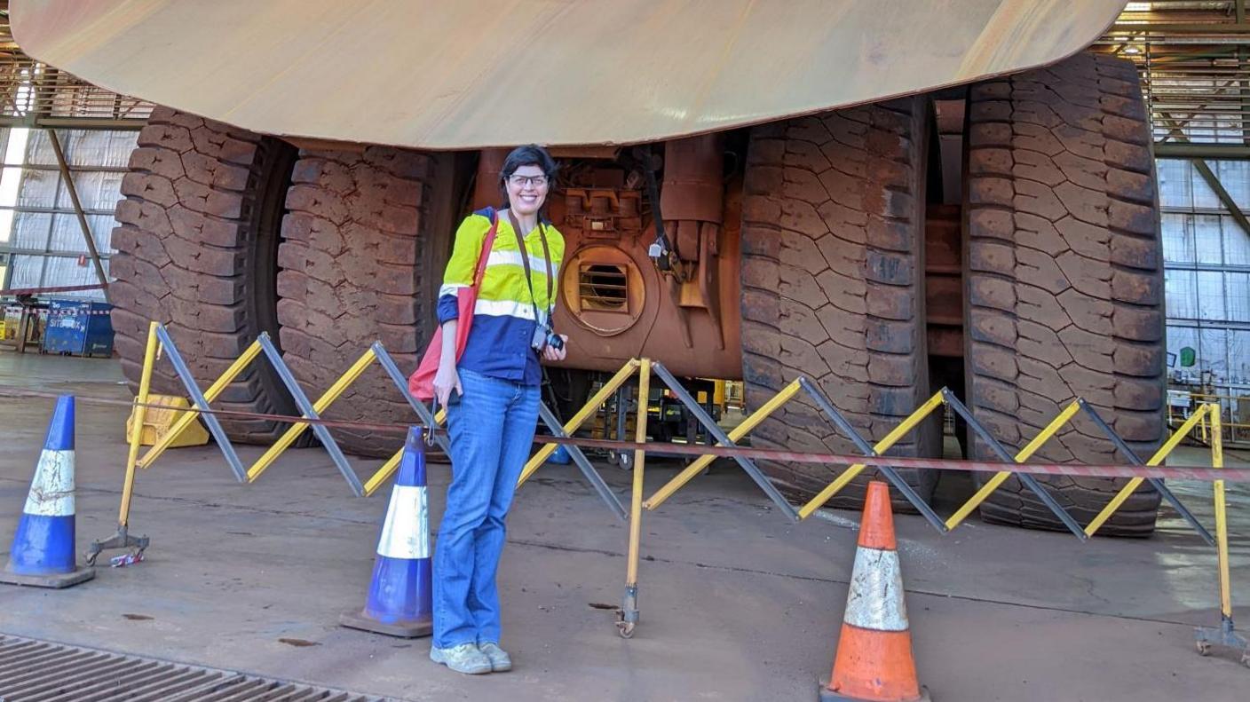 Zoe standing next to a mining truck. The wheels look taller than her.