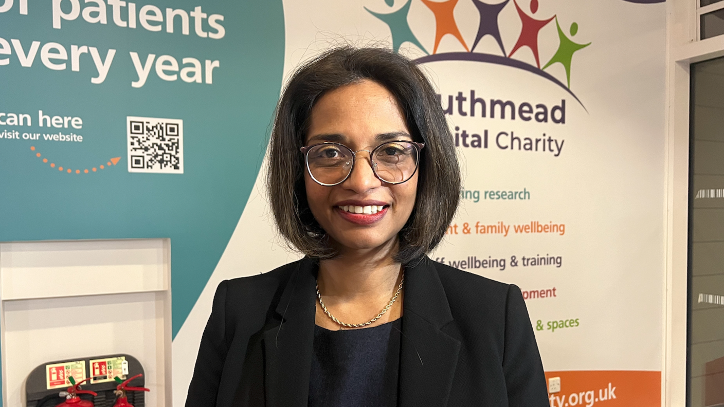 Dr Kathreena Kurian standing in front of Southmead Hospital Charity logo.