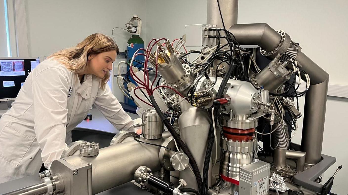 Madeline Berrow looking into an analytical machine which can test the bacteria-killing effectiveness of their paint.