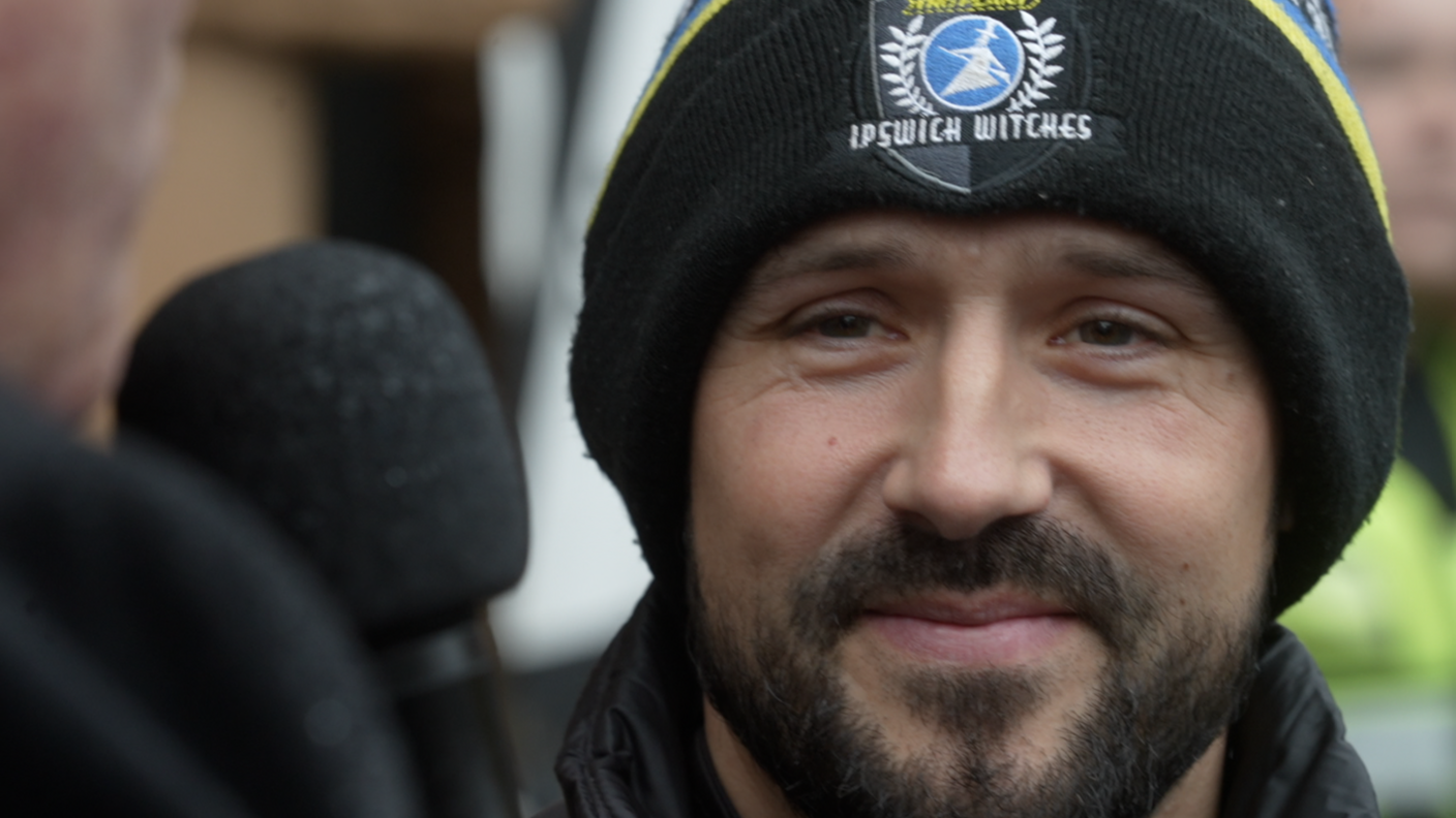 A close up of Danny King as he is interviewed. He wears a black beanie hat with Ipswich Witches' logo on it. He has a dark black beard.
