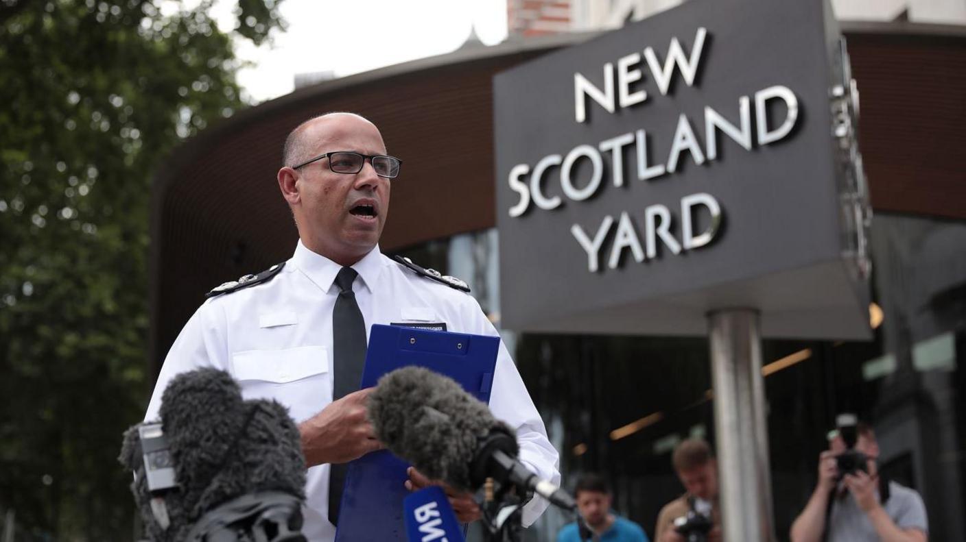 Neil Basu at New Scotland Yard reading a statement to the media outside New Scotland Yard on July 9, 2018 in London, England. He is wearing police uniform and there is a large sign for New Scotland Yard behind him. 