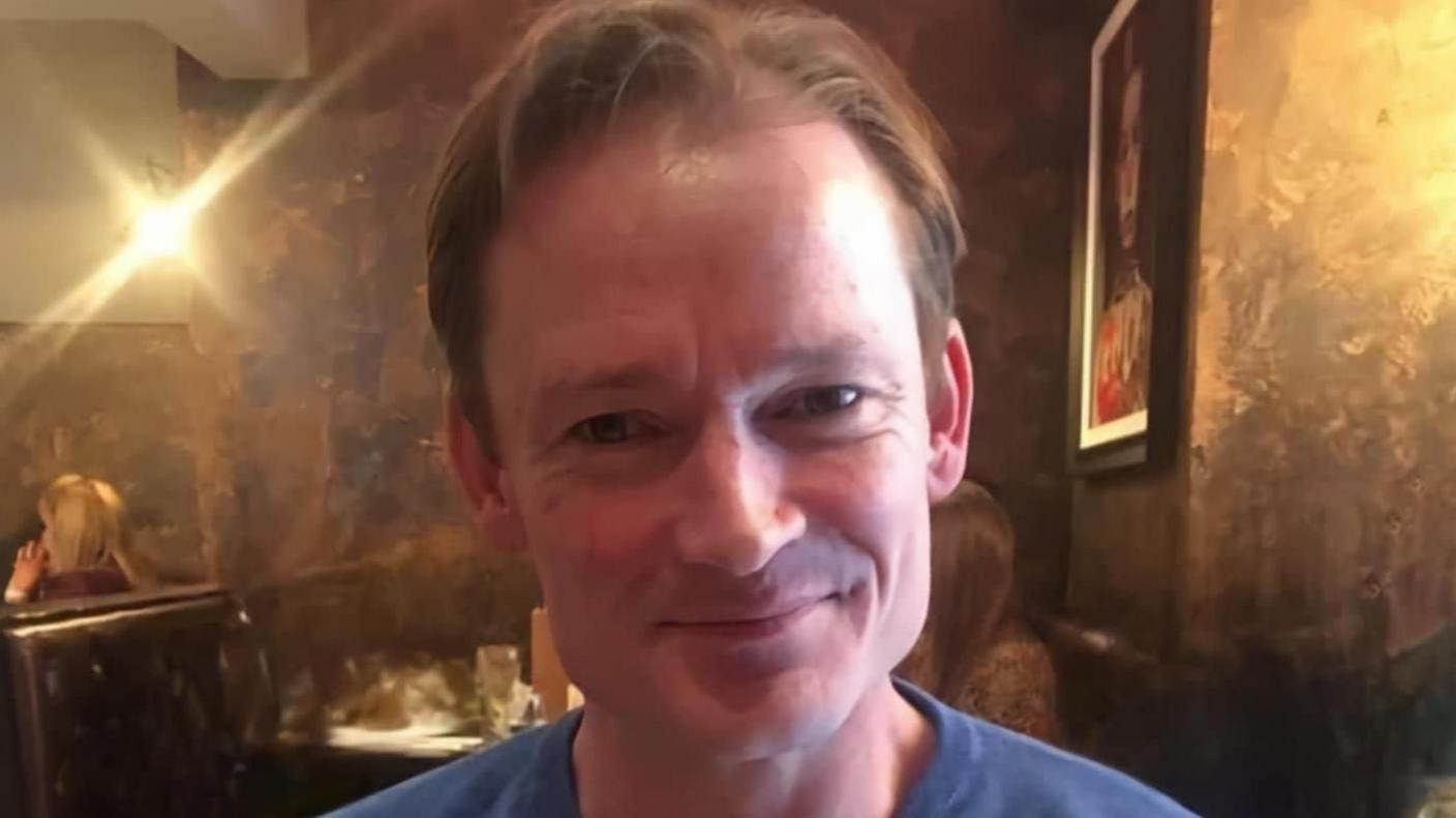 A smiling Graham Green, pictured in what appears to be a dimly lit restaurant. 