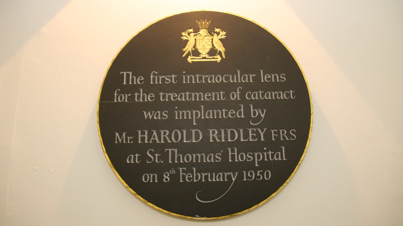 An etched grey plaque with a gold border sits on a wall in Guy's & St Thomas' Hospital, reading: " The first intraocular lens for the treatment of cataract was implanted by Mr Harold Ridley at St Thomas' Hospital on 8 February 1950'