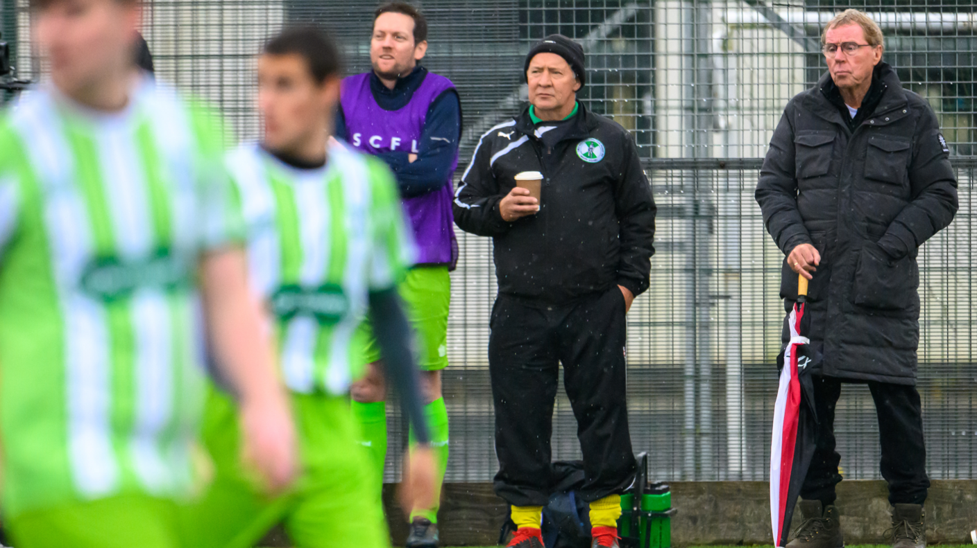 Harry Redknapp on the sidelines standing next to the permanent coach, with a couple of blurred footballers in the foreground in play