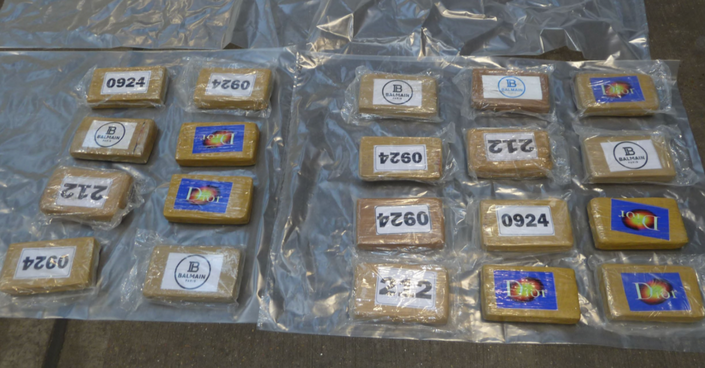 A large number of bags of drugs, laid out on a surface, with plastic sheeting around them. They have numbers and names written on them. The bags look yellow in colour. 